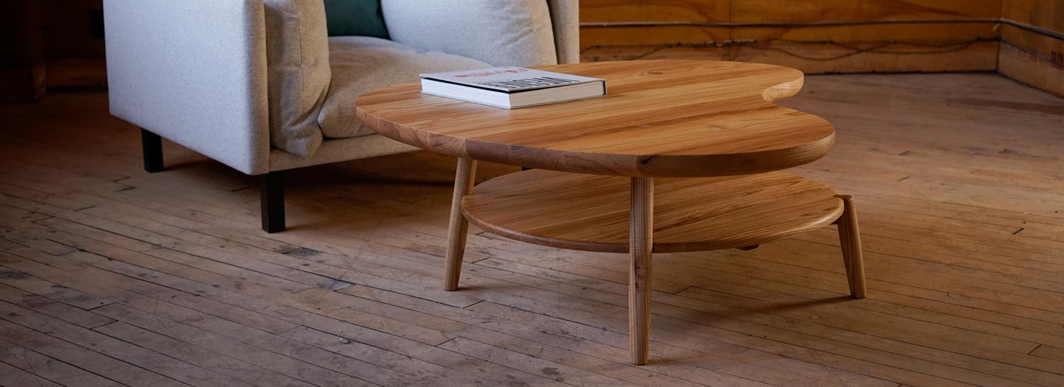 A custom coffee table with an organic shape, sitting infront of a big easy chair with a book on top.