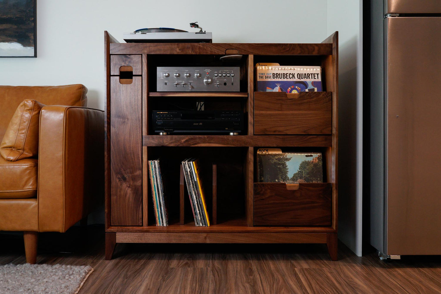 A walnut record cabinet, filled with records and stereo equipment, next to a leather couch.