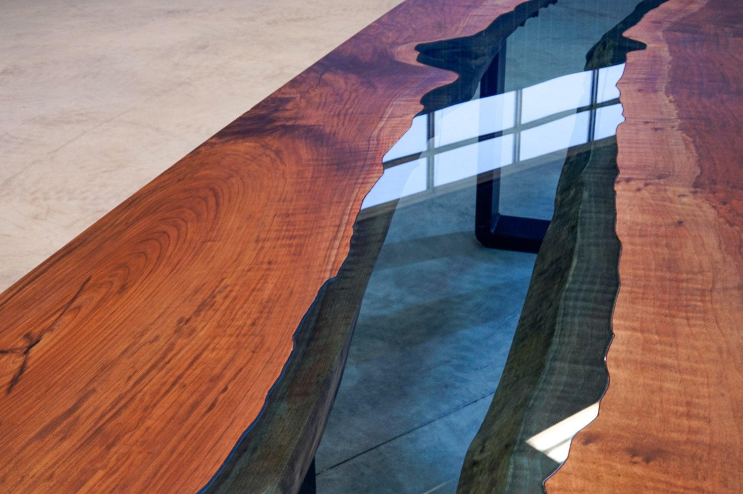 Looking down at the glass river of a custom river table, with reflections of windows in the blue tempered glass.