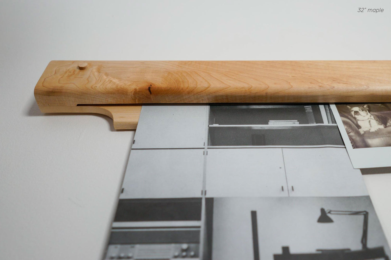 The Gravity Bar, by Biglow Woodcraft; a wooden holder for papers, pictures and images. Wooden bar installed on a white wall, holding a black and white photo of a kitchen. Hardwood Maple