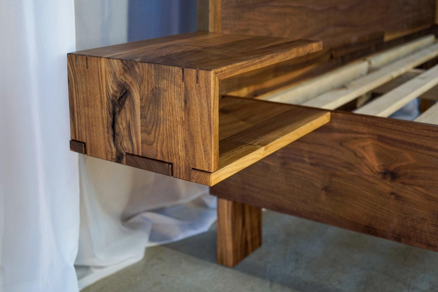 A closeup of the integrated bedside table of a custom walnut bedframe. Large finger joints and a waterfall miter joint is used.