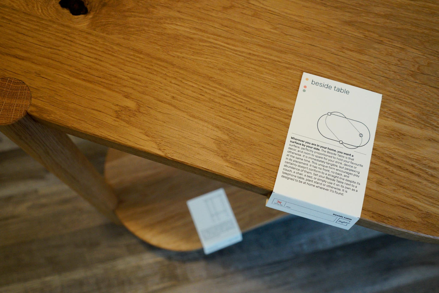 The Beside Table, by Biglow Woodcraft; close up of a wooden table with the label. Hardwood White Oak