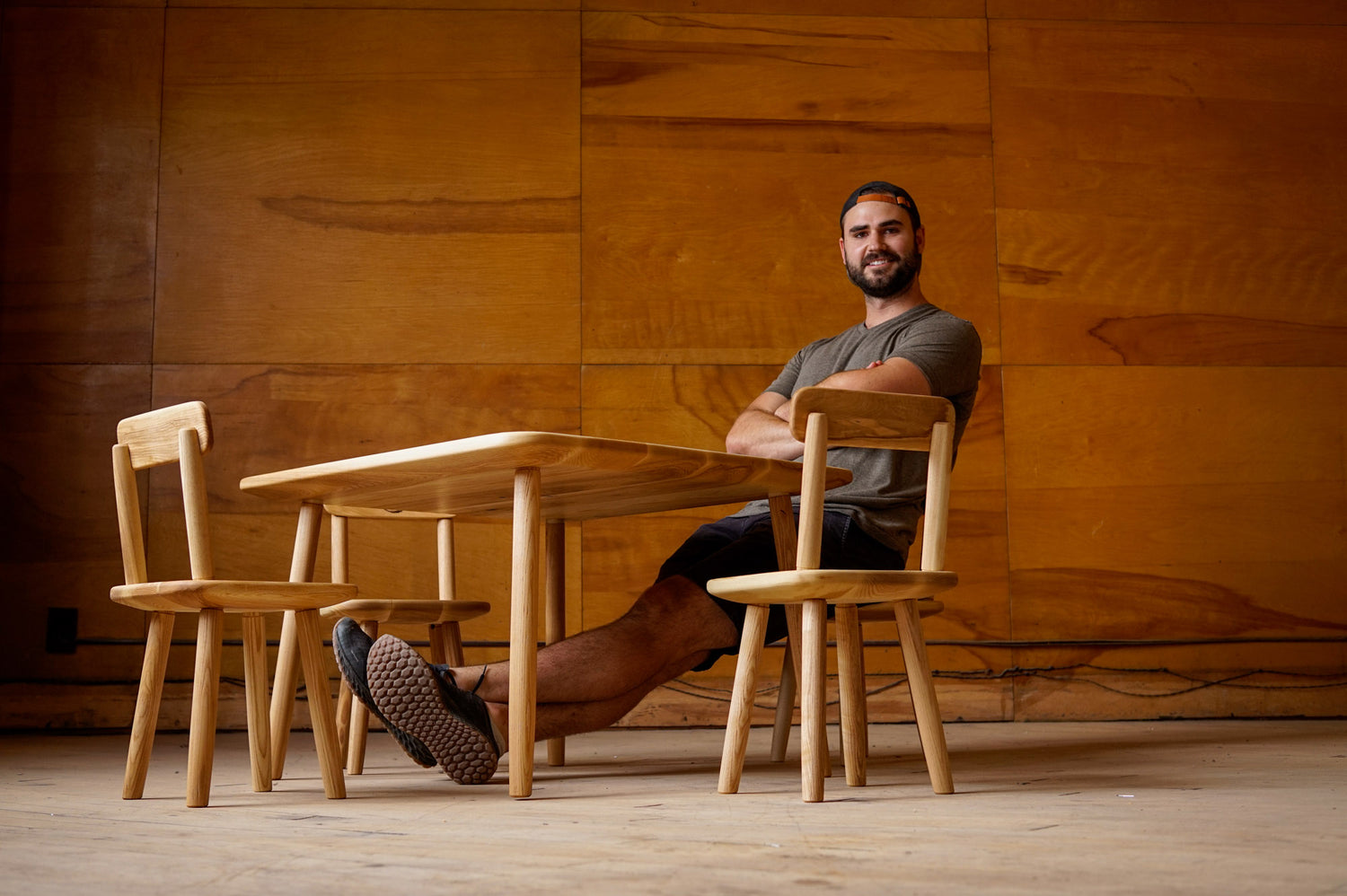 Brent Biglow sitting at the comically small children's dining set that he made, legs and arms crossed, very casual.