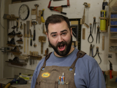 Man in a workshop wearing an apron with fine woodworking tools in the background
