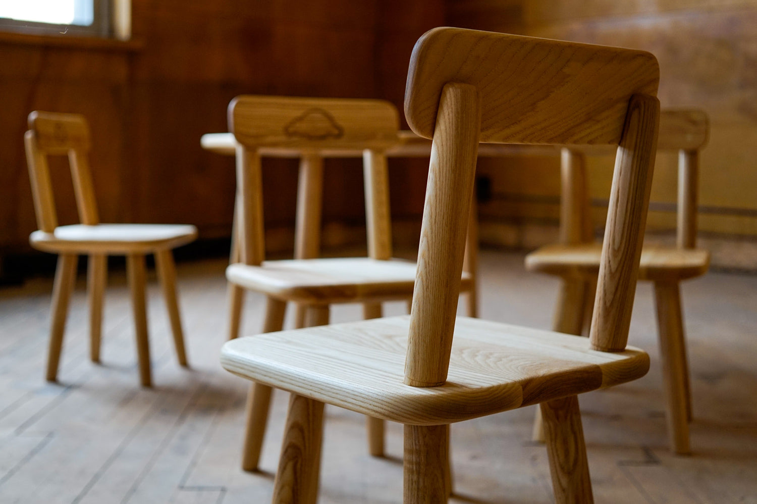 A closeup of the back of a custom children's chair, with the 3 other chairs and table in the background, blurry.