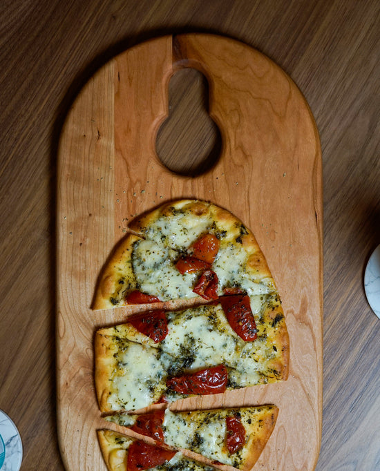 Biglow Woodcraft Food Board sitting with a flatbread pizza on top and oregano sprinkled all over.