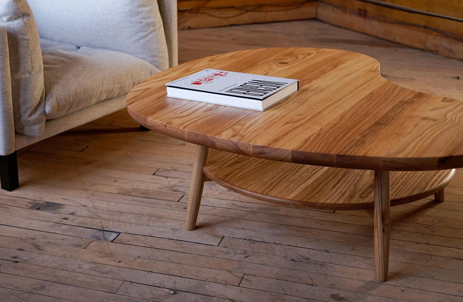 An organic shaped hardwood coffee table with a design book on top.