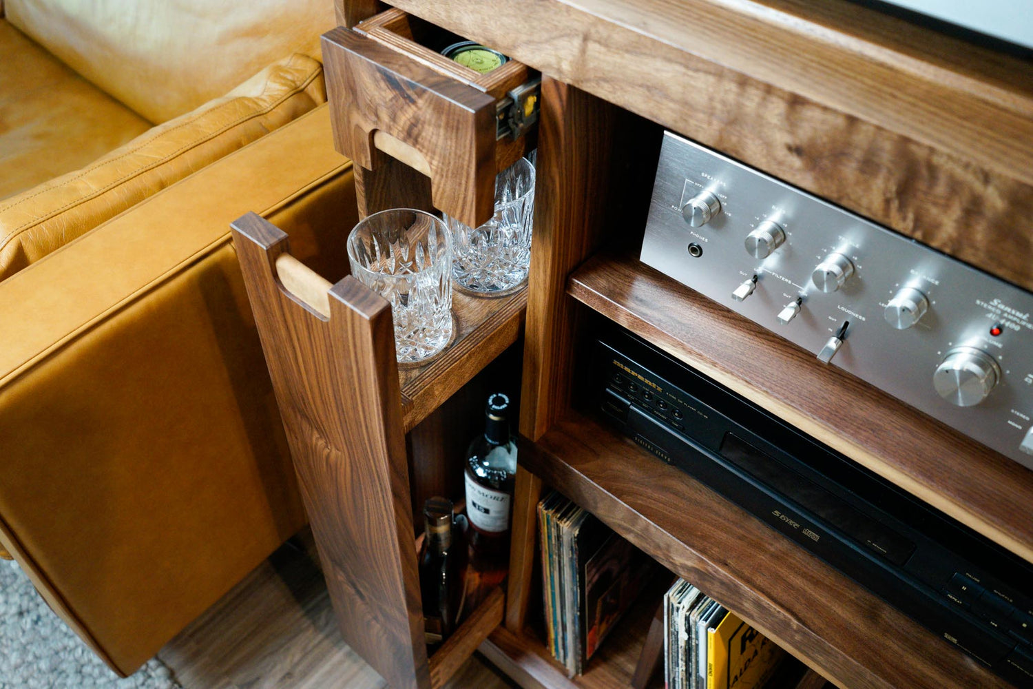 A detail shot of a custom record cabinet, showing 2 of it's drawers partially open. Once containing record maintenance tools, and the other holding whiskey glasses and various alcohol bottles.