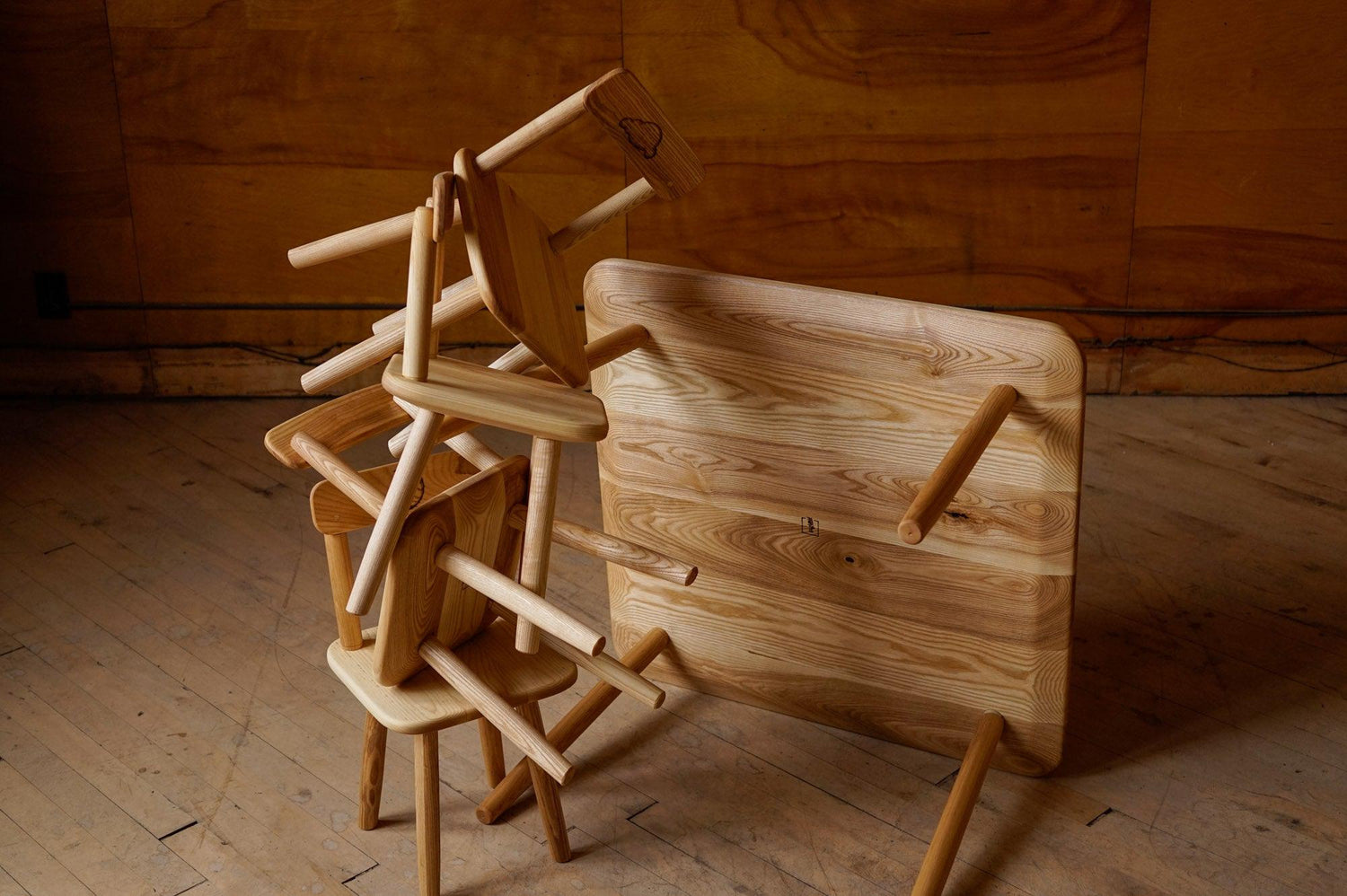 A custom children's dining set, with the chairs stacked erratically, as if children did the stacking. They are positioned in front of the table which is turned up on its side, showing the bottom.