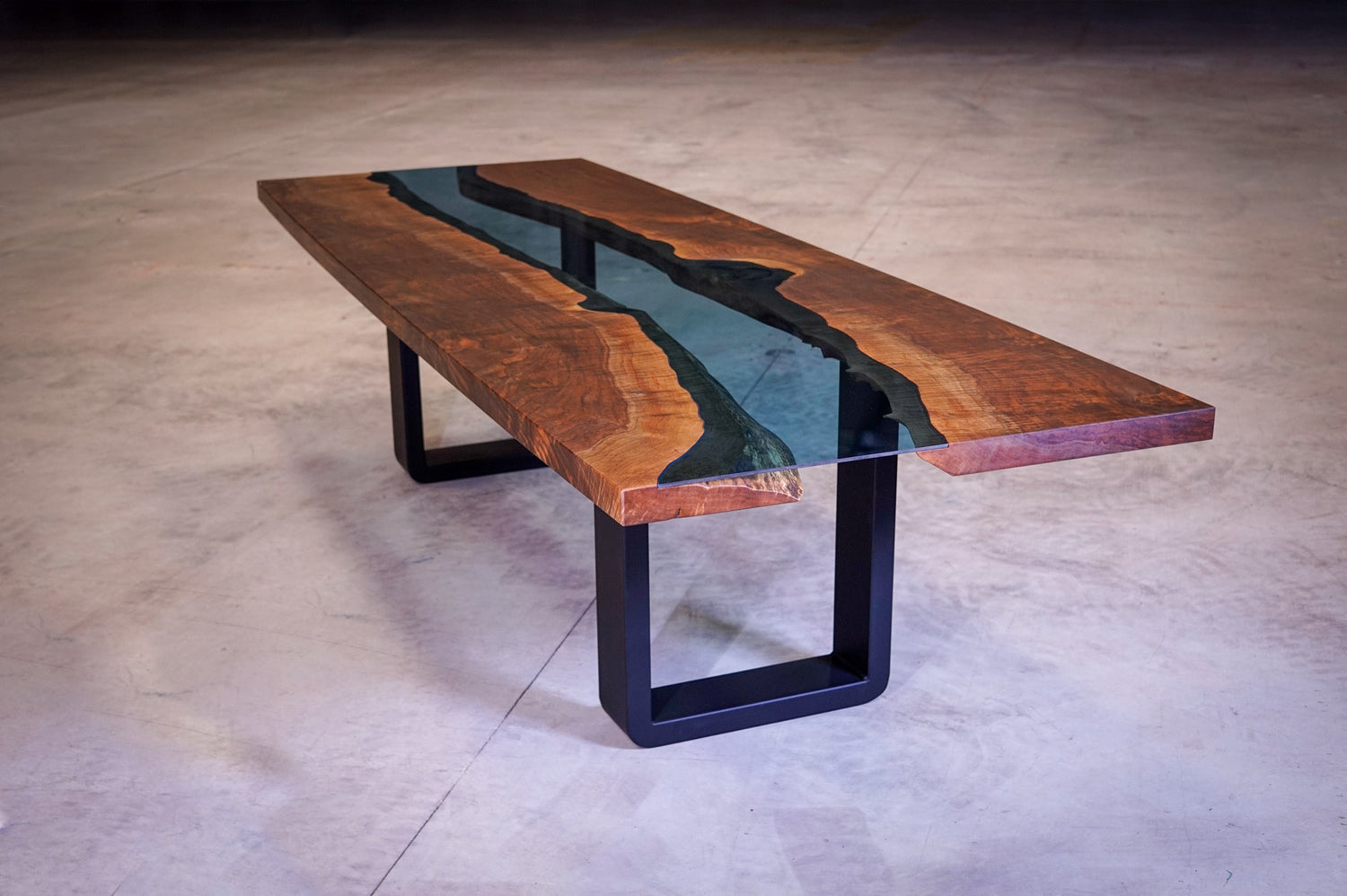 A distant shot of a large custom glass river table, orangey brown walnut slabs on either side, with a custom piece of blue tempered glass inlaid down the middle.