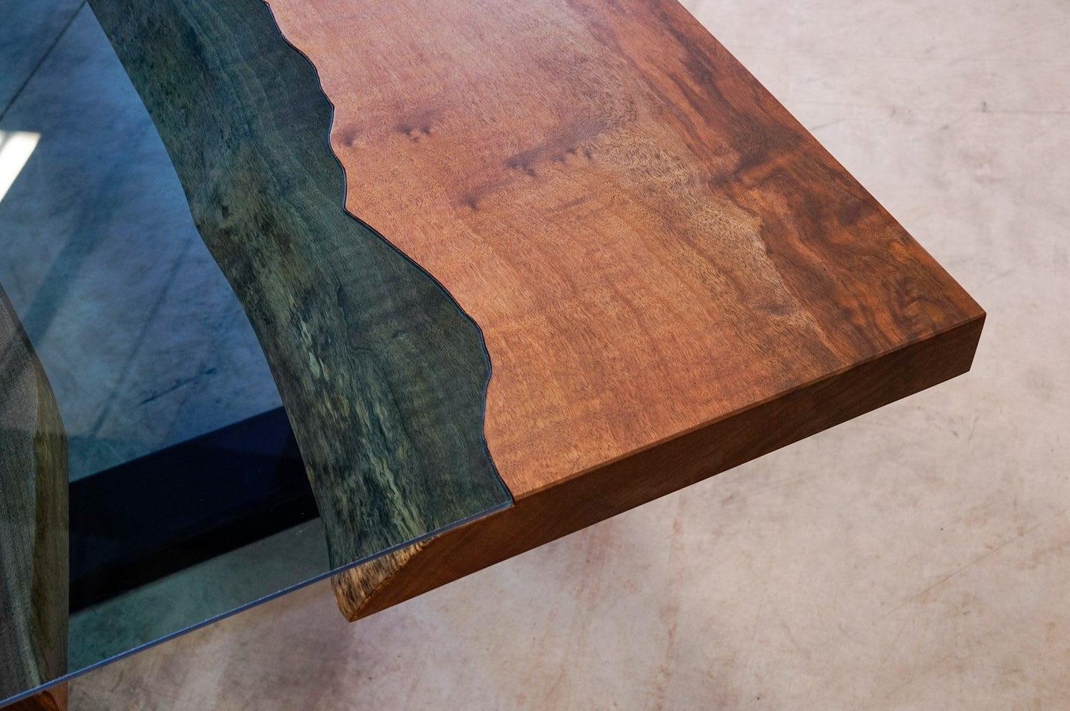 The corner of a tempered glass river table, viewing the seam between the glass and wood.