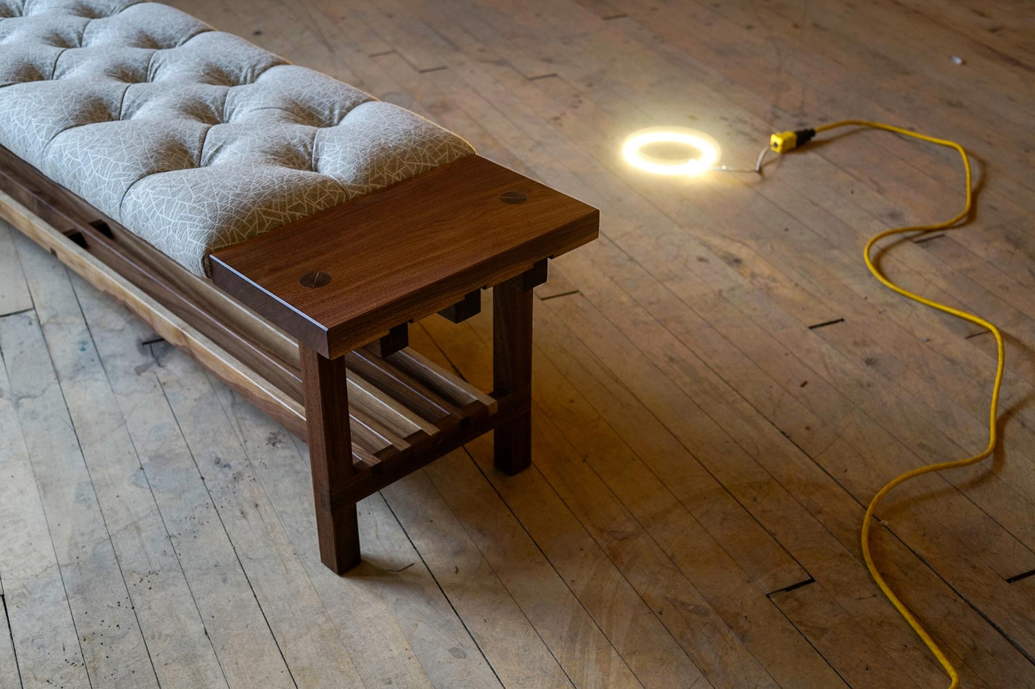 A custom bench with fine joinery, lit from behind with a visible light sitting on the floor with the cord running along the edge of the photo.