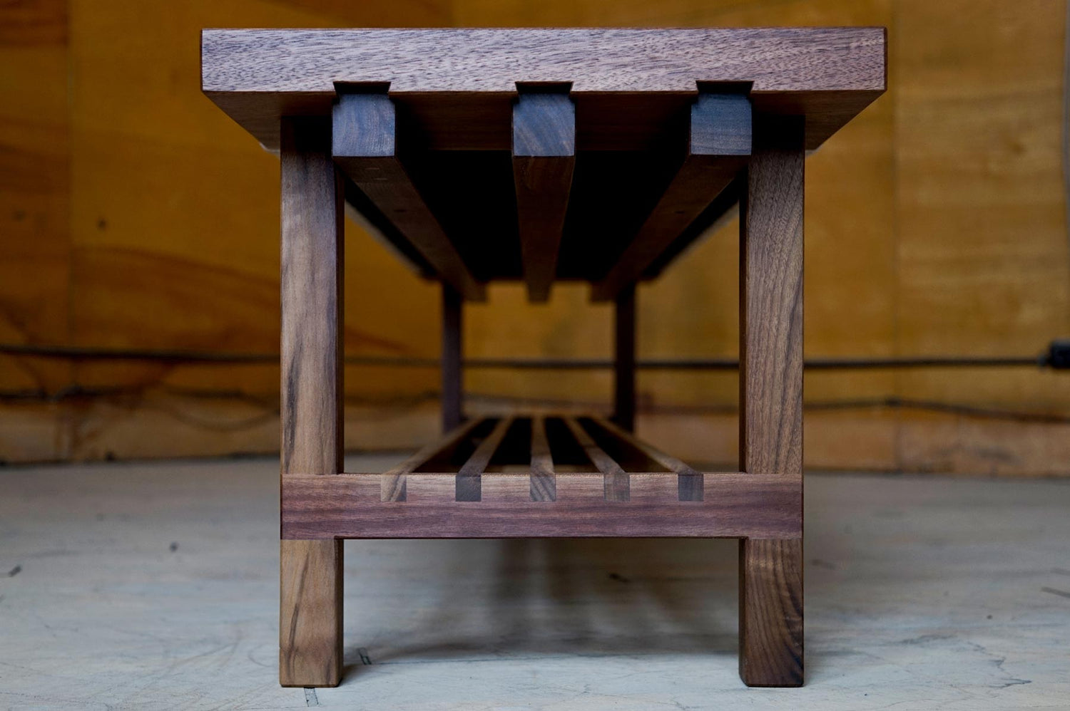 A side view of a custom walnut bench, showing some half lap joints for the lower shelf, and sliding dovetail rails that support the seat cushion.
