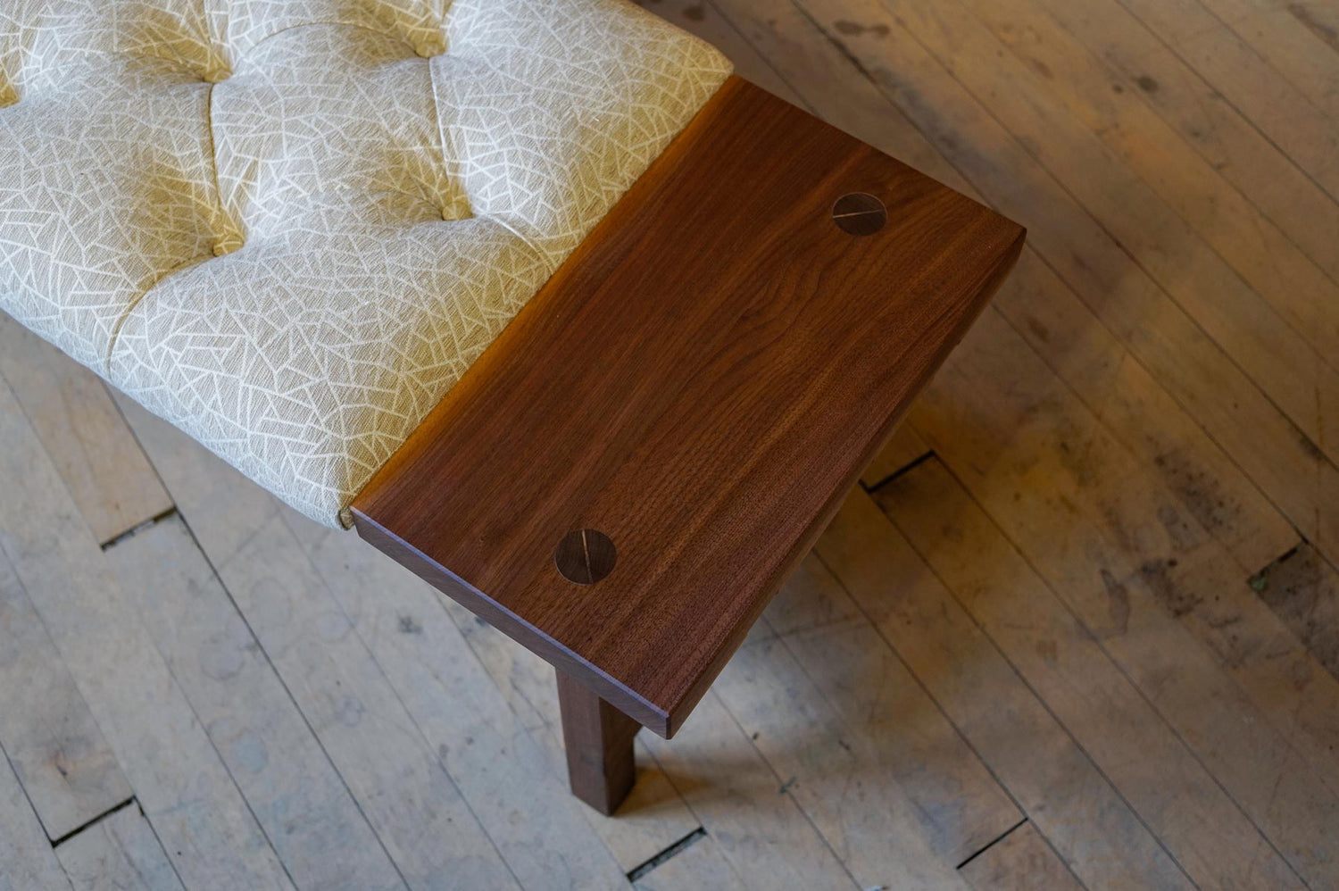 Looking down at the seam between a custom upholstered cushion and the walnut wood surface next to it on a custom designed bench.